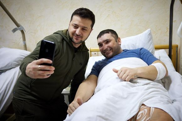 볼로디미르 젤렌스키(왼쪽) 우크라이나 대통령이 13일(현지시간) 수도 키이우(키예프)의 한 병원을 방문해 부상병과 휴대전화로 셀카를 찍고 있다.  우크라 대통령실 제공·AP 연합뉴스