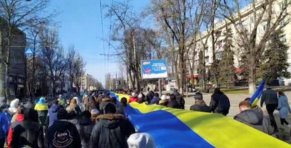 러시아의 우크라이나 침공에 항의하는 사람들이 헤르손에서 시위를 벌이고 있다. 생방송으로 중계된 영상은 13일 우크라이나 헤르손에서 러시아의 우크라이나 침공에 항의하는 사람들이 우크라이나 국기의 색깔로 된 현수막을 들고 있는 모습을 담고 있다. 로이터 연합뉴스 2022-03-14