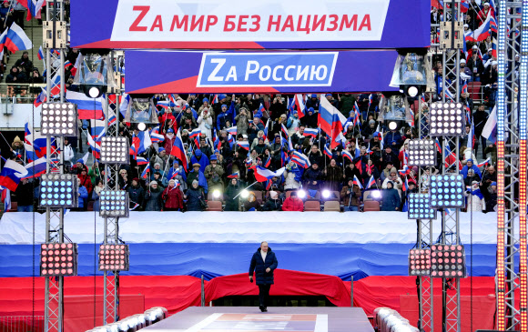 블라디미르 푸틴 러시아 대통령이 18일(현지시간) 모스크바 루즈니키 경기장에서 열린 크림반도 병합 8주년 기념 콘서트 연단에 오르고 있다. 무대 뒤로 ‘러시아를 위하여’, ‘나치즘 없는 세상을 위하여’ 등 문구가 보인다.  모스크바 타스 연합뉴스