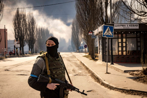 24일(현지시간) 우크라이나 수도 키이우 교외의 불타는 창고 근처에서 우크라이나 병사 1명이 주변을 경계하고 있다. AFP 연합뉴스