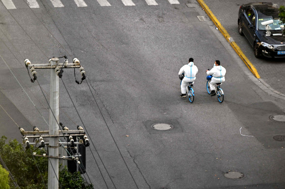 방호복을 입은 방역요원들이 코로나19 확산 방지를 위한 도시 봉쇄로 한산해진 중국 상하이 징안구의 한 거리를 자전거를 타고 지나고 있다. 2022.4.9 AFP 연합뉴스