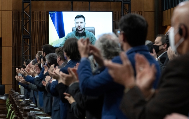 15일(현지시각) 캐나다 수도 오타와의 의사당에서 의원들과 초청 인사들이 대형 모니터 화면에 볼로디미르 젤렌스키 우크라이나 대통령이 화상 연설을 하기 위해 등장하자 기립 박수를 보내고 있다. 연합뉴스