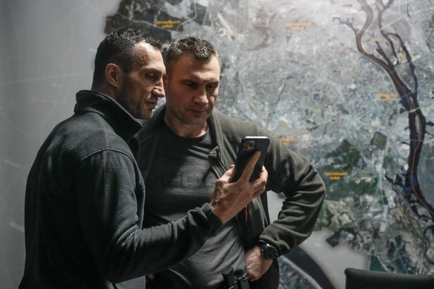 우크라이나 키이우 시장인 전 헤비급 세계 챔피언 비탈리 클리츠코(오른쪽)와 그의 동생 블리디미르 클리츠코가 키이우 시청에서 스마트폰을 보며 이야기를 나누고 있다.AP 연합뉴스