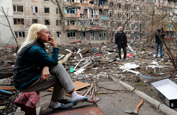 우크라이나 남부 항구도시 마리우폴에서 18일(현지시간) 한 여성이 러시아군의 무차별 폭격으로 파괴된 주거단지 앞마당에 망연자실한 표정으로 앉아 있다. 6주 넘게 러시아군의 포위 공격을 받은 마리우폴은 도시 기반시설의 90% 이상이 파괴돼 이곳 주민들은 식량, 식수, 전기 공급이 끊긴 채 하루하루를 연명하고 있다. 2022.4.19 마리우폴 로이터 연합뉴스