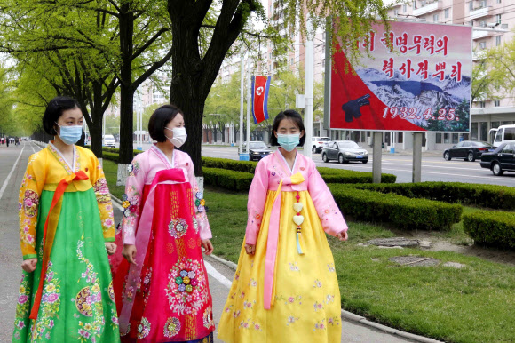 북한 조선인민혁명군(항일 빨치산) 창건 90주년인 25일 한복을 입은 평양 여성들이 길가에 세워진 경축 포스터 곁을 지나고 있다. AP 연합뉴스