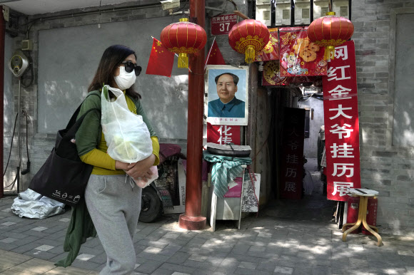 중국의 수도 베이징이 고강도 방역 조치에도 하루 수십명씩 신규 감염자가 쏟아져 어려움을 겪고 있는 가운데 지난 3일 한 시민이 마스크를 하고 마오쩌둥 초상화가 걸린 가게 앞을 지나고 있다. 베이징 AP 연합뉴스