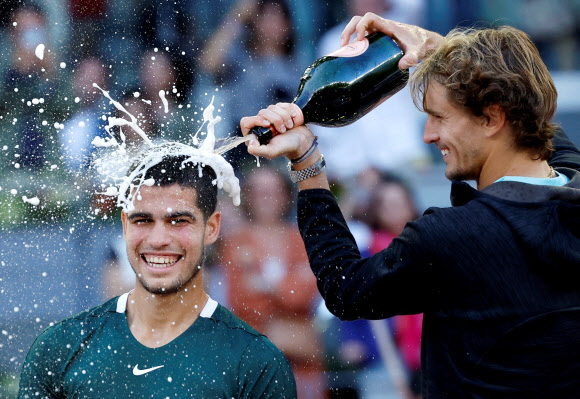 카를로스 알카라스가 8일 남자프로테니스(ATP) 투어 마드리드오픈에서 우승한 뒤 결승 상대였던 알렉산더 츠베레프가 자신의 머리에 부어주는 샴페인을 맞으며 익살스럽게 웃고 있다. [로이터 연합뉴스]