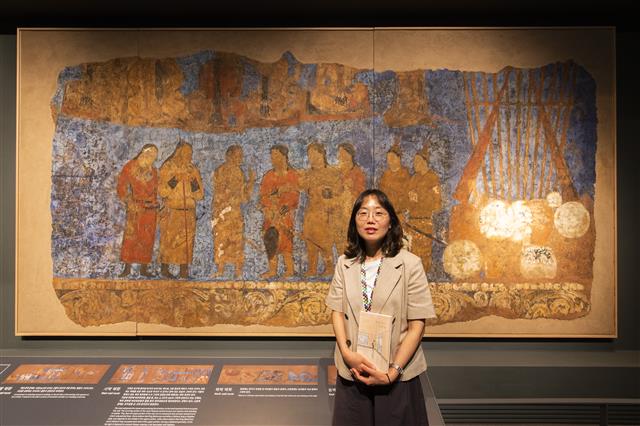 정명희 큐레이터가 서울 용산구 국립중앙박물관에 전시된 작품이자 자신의 책에 소개된 ‘사마르칸트 아프라시아브 궁전 유적 벽화 모사도’ 앞에서 미소 짓고 있다.