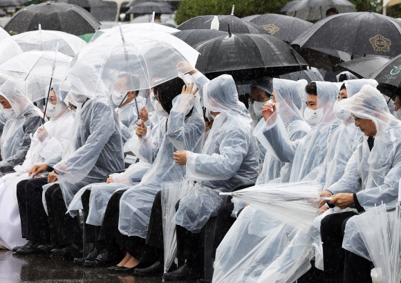 윤석열 대통령이 6일 서울 동작구 국립서울현충원에서 열린 제67회 현충일 추념식에서 부인 김건희 여사의 우비 모자를 씌어주고 있다.2022.6.6   박지환 기자