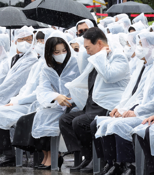 윤석열 대통령 부인 김건희 여사가 6일 서울 동작구 국립서울현충원에서 열린 제67회 현충일 추념식에서 윤 대통령의 우비 착용을 돕고 있다.  2022. 6. 6  박지환 기자