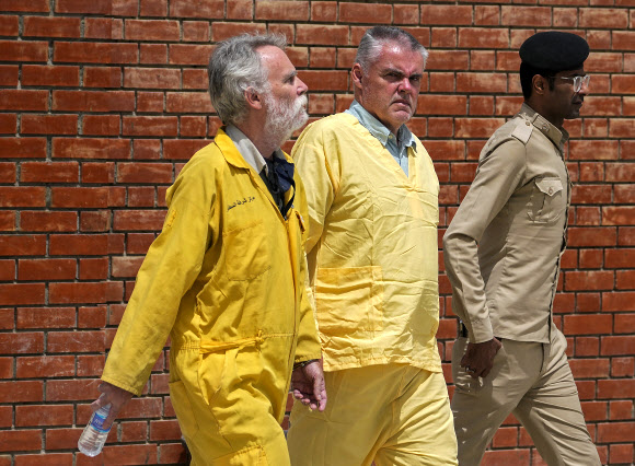 지난달 22일 이라크 바그다드의 법정 밖에서 영국의 짐 피튼(사진 왼쪽)이 수감자들의 노란색 제복을 입고 이라크 보안군의 호위를 받고 있다. AP통신