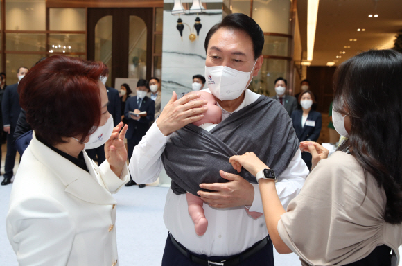 윤석열 대통령이 5일 오후 서울 여의도 중소기업중앙회관에서 제1회 여성기업주간 ‘여성경제인의 날 유공자 정부포상 수여식’에 참석하기 전 육아용품 브랜드 코니바이에린 부스에서 아기띠를 매어보고 있다. 2022.7.5  대통령실사진기자단