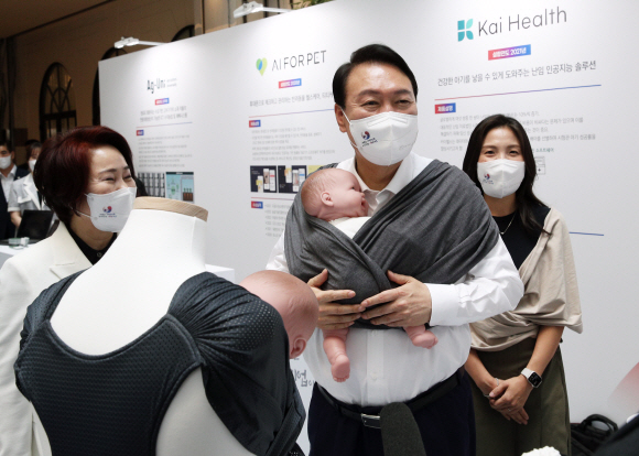 윤석열 대통령이 5일 오후 서울 여의도 중소기업중앙회관에서 제1회 여성기업주간 ‘여성경제인의 날 유공자 정부포상 수여식’에 참석하기 전 육아용품 브랜드 코니바이에린 부스에서 아기띠를 매어보고 있다. 2022. 6. 29  박윤슬 기자