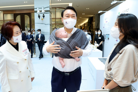 윤석열 대통령이 5일 서울 여의도 중소기업중앙회관에서 열린 ‘제1회 여성기업 개막식’에 앞서 육아용품 업체인 코니바이에린 부스를 방문해 아기띠를 직접 착용해보고 있다.  2022.7.5  연합뉴스