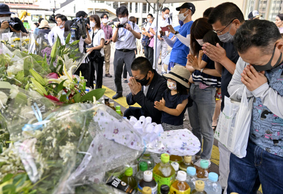 People pray at a makeshift memorial near the scene where the former Prime Minister Shinzo Abe was shot while delivering his speech to support the Liberal Democratic Party‘s candidate during an election campaign in Nara, Saturday, July 9, 2022.  Abe, a divisive arch-conservative and one of his nation’s most powerful and influential figures, has died after being shot during a campaign speech Friday in western Japan, hospital officials said. AP 연합뉴스