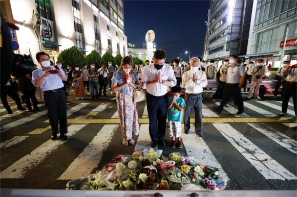 People pray at a makeshift memorial at the scene where the former Prime Minister Shinzo Abe was shot while delivering his speech to support the Liberal Democratic Party‘s candidate during an election campaign in Nara, Friday, July 8, 2022.  Abe, a divisive arch-conservative and one of his nation’s most powerful and influential figures, has died after being shot during a campaign speech Friday in western Japan, hospital officials said. AP 뉴시스