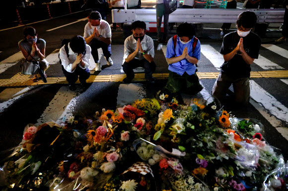 아베 신조 전 일본 총리가 참의원 선거 유세 도중 총격을 받고 사망한 8일 나라현 나라시 야마토사이다이지역 앞에 그의 죽음을 애도하는 꽃이 수북이 쌓인 가운데 시민들이 두 손을 모아 명복을 빌고 있다. 2022.7.8 로이터 연합뉴스