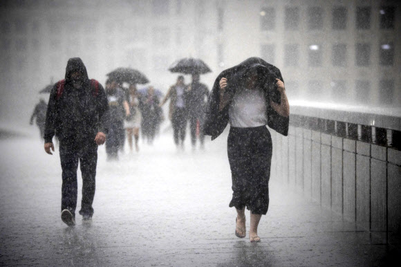 지구촌이 극단적인 이상기후로 신음하고 있다. 17일(현지시간) 영국에서는 일부 지역에서 최대 100㎜에 달하는 폭우가 쏟아진 가운데 우산을 준비하지 못한 시민들이 외투를 뒤집어쓴 채 런던 브리지를 건너고 있다. 런던 EPA 연합뉴스