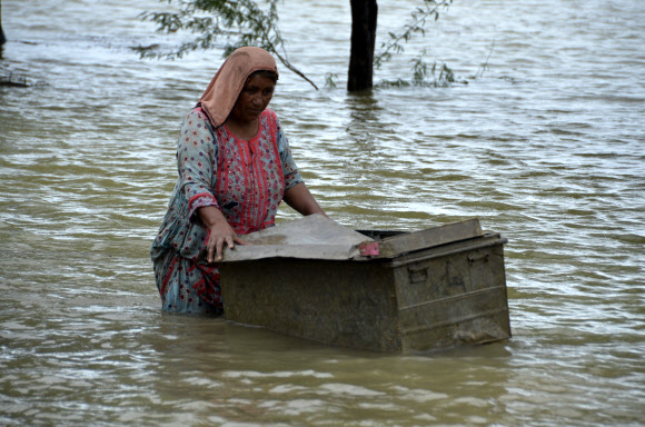 25일(현지시간) 파키스탄 남서부 발루치스탄 주의 자프라바드에서 한 여성이 홍수 피해를 입은 집에서 쓸 수 있는 물건들을 건져내기 위해 여행용 가방을 물 위로 옮기고 있다. 파키스탄 정부는 올 석달 가까이 이어진 폭우로 큰 피해를 입자 국제 사회의 지원을 요청했다. 자프라바드 AP 뉴시스 
