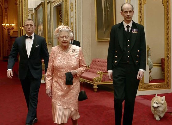 2012년 7월 29일 제임스 본드 역으로 유명한 영국 배우 대니얼 크레이그(왼쪽)가 2012 런던 올림픽 개막식에서 엘리자베스 2세(가운데) 여왕을 호위하고 있는 모습. 반려견 코기가 이를 뒤따르고 있다. AFP 연합뉴스