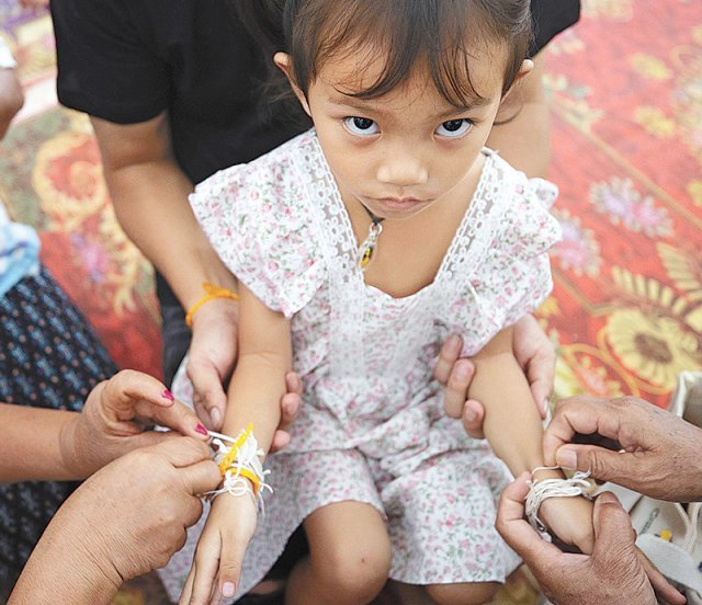 8일 태국 북동부 우타이사완의 사원에서 이틀 전 발생한 어린이집 총기 난사 사건 희생자의 친척들이 희생자의 평안을 기리는 의미로 유일한 생존자 빠위눅 수폴웡(3)의 손에 실을 묶고 있다. AP 뉴시스