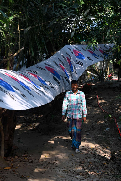 태극기 띠를 만들어 한국축구를 응원하는 방글라데시인 아부 코시르가 반샤람푸르의 마을과 마을을 잇는 도로와 다리 위를 장식한 3.5㎞ 길이의 태극기 띠 앞에서 걸어오고 있다. 지난 16일(현지시간) 촬영됐다. 반샤람푸르 AFP 연합뉴스 