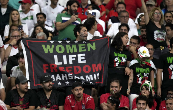 이란 축구팬들이 2022년 11월 21일 카타르 도하 칼리파 국제경기장에서 열린 월드컵 B조 잉글랜드와 이란의 축구경기에 앞서 ‘Woman Life Freedom Masha Amin’i라고 적힌 팻말을 들고 있다. 2022.11.22 AP 연합뉴스