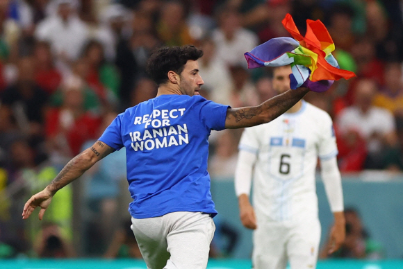 H조 - 포르투갈 대 우루과이 - 루사일 스타디움, 카타르, 루사일 - 2022년 11월 28일 경기 도중 이란 여성을 응원하는 셔츠를 입은 관중이 무지개 깃발을 들고 그라운드를 달리고 있다. REUTERS/Matthew Childs