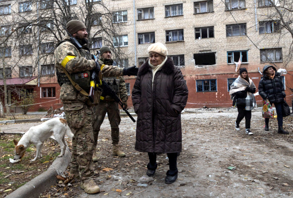 11일(현지시간) 러시아군의 공습으로 파괴된 우크라이나 동부 헤르손에 있는 건물 앞에서 우크라이나군이 한 여성과 대화하고 있다. 헤르손 로이터 연합뉴스