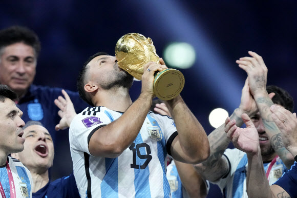 지난해 은퇴한 아르헨티나 축구 스타 세르히오 아구에로가 19일(한국시간) 리오넬 메시를 비롯해 대표팀 후배들이 프랑스를 승부차기 끝에 물리치고 36년 만에, 사상 세 번째 차지한 우승 트로피에 입을 맞추는 퍼포먼스를 하고 있다. 루사일 AP 연합뉴스 