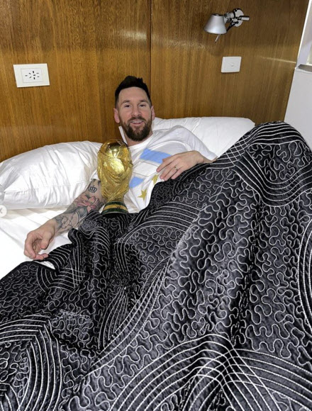 In this handout picture posted on the official Instagram account of @leomessi, Argentina‘s captain and forward Lionel Messi poses in bed with the FIFA World Cup Trophy at the Argentine Football Association (AFA) training centre in Ezeiza, Buenos Aires province, Argentina, on December 20, 2022. - Argentina captain Lionel Messi posts a series of photos on his Instagram page of himself hugging the World Cup Trophy in bed. AFP 연합뉴스