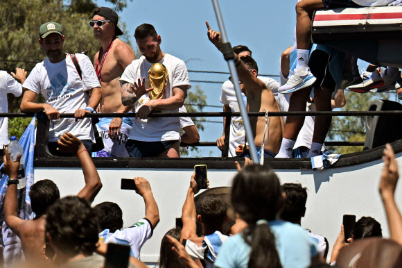 Argentina‘s Lionel Messi waves at fans holding the FIFA World Cup Trophy as the team parades on board a bus after winning the Qatar 2022 World Cup tournament in Buenos Aires province, Argentina on December 20, 2022. - Millions of ecstatic fans are expected to cheer on their heroes as Argentina’s World Cup winners led by captain Lionel Messi began their open-top bus parade of the capital Buenos Aires on Tuesday following their sensational victory over France. AFP 연합뉴스