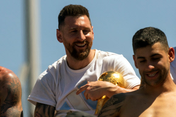 Argentina‘s Lionel Messi (L) holds the FIFA World Cup Trophy as the team parades on board a bus after winning the Qatar 2022 World Cup tournament in downtown Buenos Aires, Argentina on December 20, 2022. - Millions of ecstatic fans are expected to cheer on their heroes as Argentina’s World Cup winners led by captain Lionel Messi began their open-top bus parade of the capital Buenos Aires on Tuesday following their sensational victory over France. AFP 연합뉴스