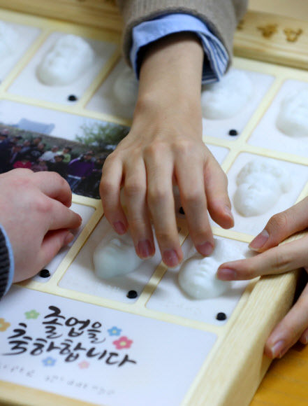 13일 대구시 남구 시각장애 학생을 위한 교육기관인 대구광명학교에서 열린 2022학년도 졸업식에서 졸업생들이 3D 프린터로 제작된 졸업앨범에서 친구 얼굴을 손끝으로 찾아보고 있다. 2023.1.13. 연합뉴스