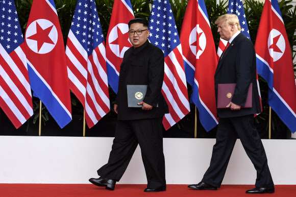 역사적 첫 북미정상회담이 열린 2018년 6월 12일(현지시간) 싱가포르 센토사 섬 카펠라호텔에서 미국 도널드 트럼프 대통령(오른쪽)과 북한 김정은 국무위원장이 공동으로 서명을 마친 합의문을 들고 나란히 걸어가고 있다. AP 연합뉴스