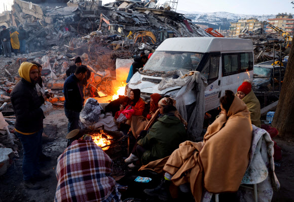 튀르키예 카흐라만마라슈에서 지진으로 피해를 입은 사람들이 무너진 건물 잔해 옆 불 주위에 담요 등을 덮은 채 앉아 있다. 2023.2.9 로이터 연합뉴스