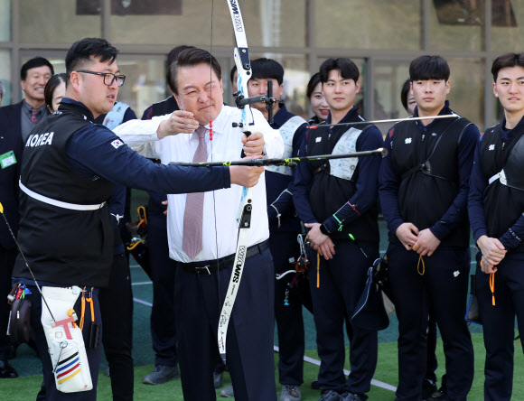 윤석열 대통령이 14일 충북 진천선수촌에서 열린 2023 대한민국 체육비전 보고회를 마친 뒤 양궁장에서 김우진 선수의 도움을 받아 화살을 쏘고 있다. 2023.2.14. 연합뉴스