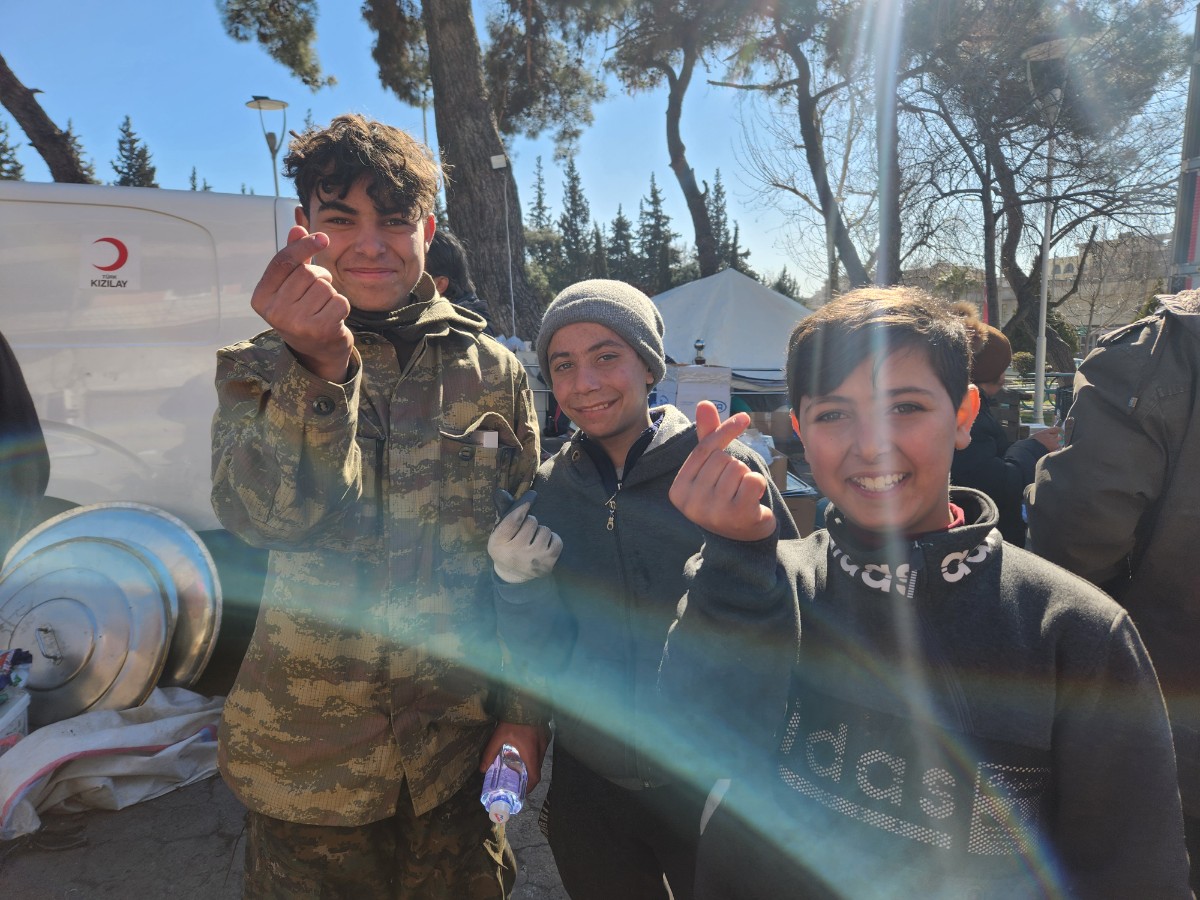지진 피해가 큰 튀르키예 카라만마라슈의 이재민 텐트촌에서 지난 13일(현지시간) 만난 시리아인 압둘라(오른쪽)와 셰이드(가운데)가 손가락 하트를 만들어 보이며 반가워하고 있다.