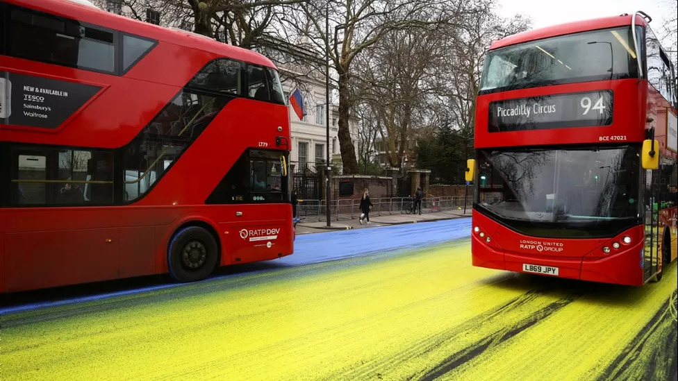 영국 런던의 2층버스들이 러시아의 우크라이나 침공 일년을 하루 앞둔 23일 아침(현지시간) 러시아 대사관 앞 도로가 우크라이나 국기 색깔인 노란색과 푸른색으로 칠해진 위를 달리고 있다. 런던 로이터 연합뉴스