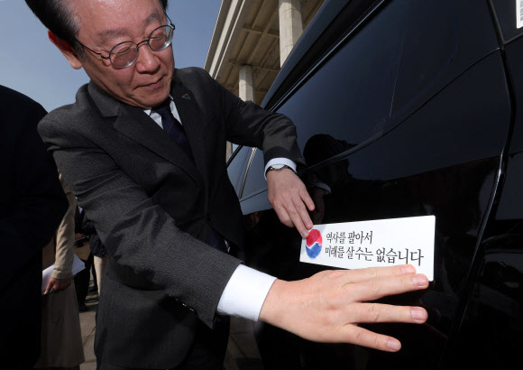 더불어민주당 이재명 대표가 22일 오전 서울 여의도 국회 본청 앞에서 열린 대일굴종외교 규탄 태극기달기 운동 행사에서 ‘역사를 팔아서 미래를 살 수는 없습니다’ 문구가 담긴 태극기 스티커를 차량에 부착하고 있다. 2023.3.22. 공동취재
