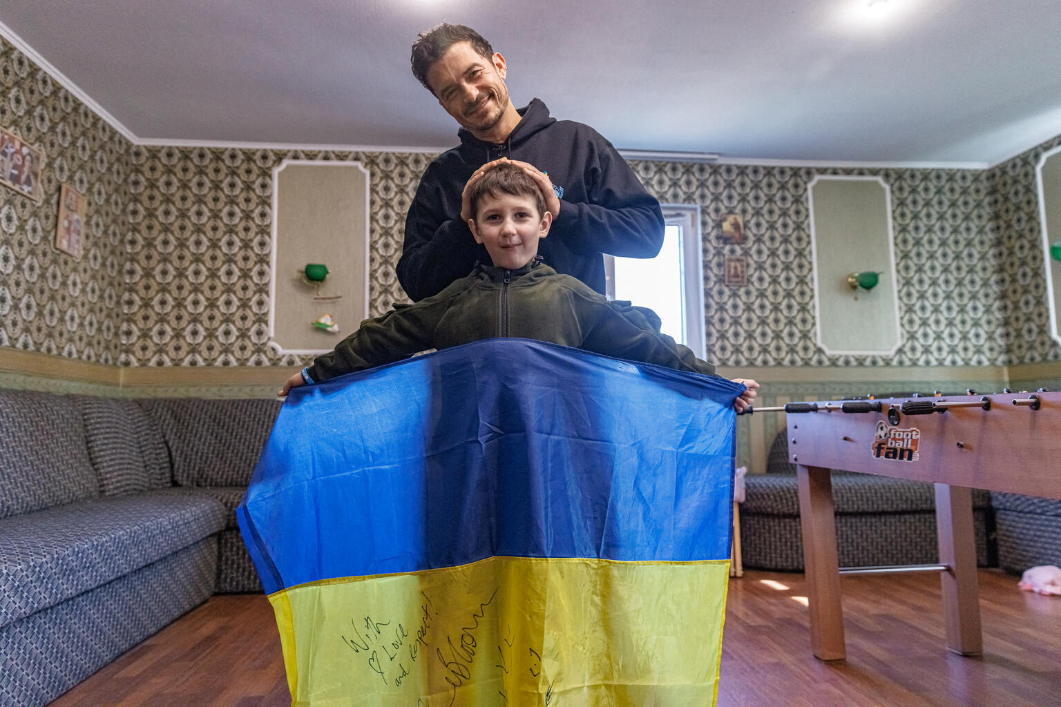유엔아동기금(UNICEF·유니세프) 친선대사인 영국 배우 올랜도 블룸이 25일(현지시간) 우크라이나 데미디프에서 현지 어린이 여호르(8)와 함께 사진을 찍고 있다. 여호르는 블룸의 서명이 담긴 우크라이나 국기를 펼쳐 들고 있다. 2023.3.26 로이터 연합뉴스
