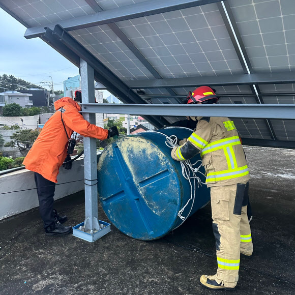 강풍을 동반한 많은 비가 내린 5일 오후 부산 영도구 한 건물 옥상에서 물탱크가 떨어지려고 해 소방당국이 안전조치에 나서고 있다. 기상청은 5일 부산에 강풍주의보와 호우주의보를 발효했다. 2023.5.6. 부산소방재난본부 제공