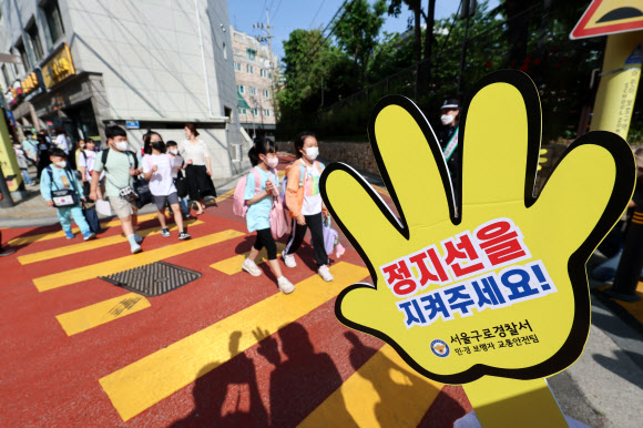 어린이들이 17일 오전 서울 구로구 덕의초등학교에서 노란색 횡단보도를 건너 등교하고 있다.  노란색 횡단보도는 운전자가 횡단보도의 색깔만으로도 어린이 보호구역임을 명확하게 인식할 수 있도록 노랗게 칠한 횡단보도로, 전국 12개 어린이 보호구역에서 3개월간 시범 운영 중이다. 2023.5.17 연합뉴스