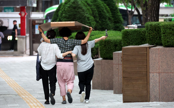 18일 서울 명동 거리에서 시민들이 내리는 비를 종이상자로 가리고 발걸음을 옮기고 있다. 2023.5.18 연합뉴스