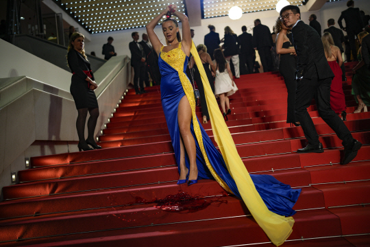우크라이나 국기와 비슷한 디자인의 드레스를 입은 한 여성이 프랑스 칸 국제영화제의 레드카펫에 오르다 붉은 액체가 든 주머니를 들어올려 자신에게 뿌리고 있다. AP 연합뉴스