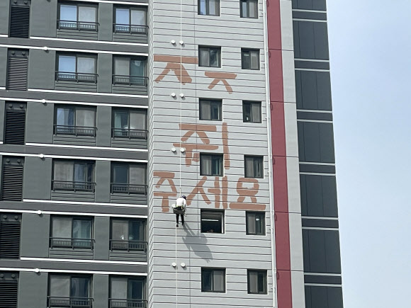 24일 오후 경기 화성시 반월동의 모 아파트에서 한 작업자가 밀린 임금을 달라며 고공 농성을 벌이고 있다. 이 작업자는 아파트 외벽에 매달려 붉은 페인트로 ‘돈 주세요’라는 글씨를 쓰기도 했다. 2023.5.24. 독자 제공·연합뉴스