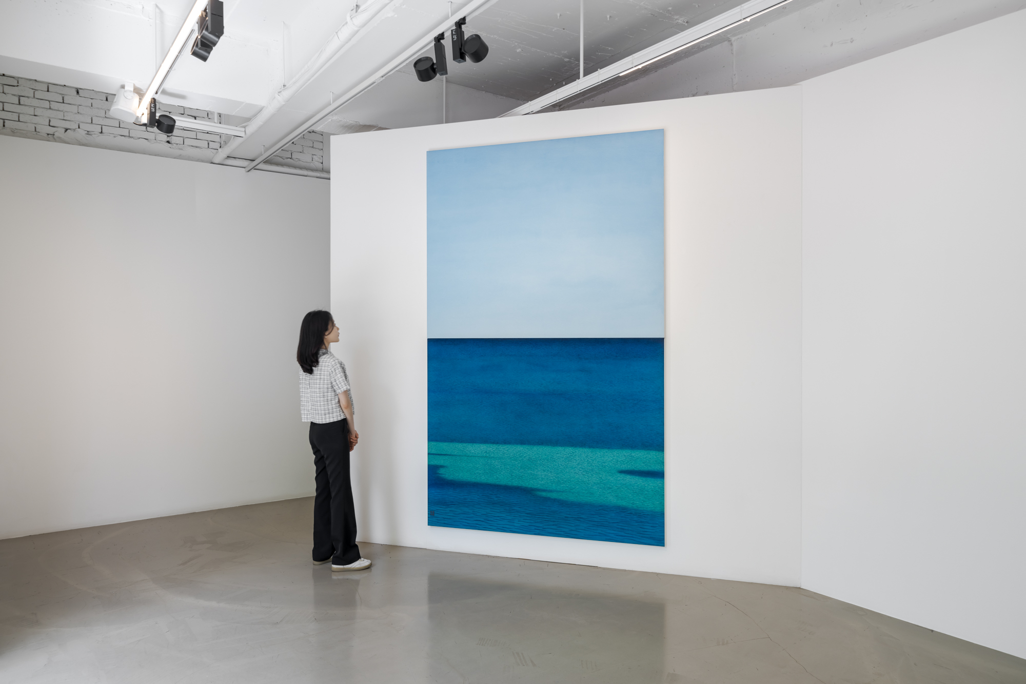김보희 작가의 개인전이 열리는 갤러리바톤을 찾은 한 관람객이 각각 하늘과 바다를 그린 캔버스 두 개를 이어 붙여 하나의 정경으로 빚어낸 ‘Towards’(2023)을 감상하고 있다. 갤러리바톤 제공
