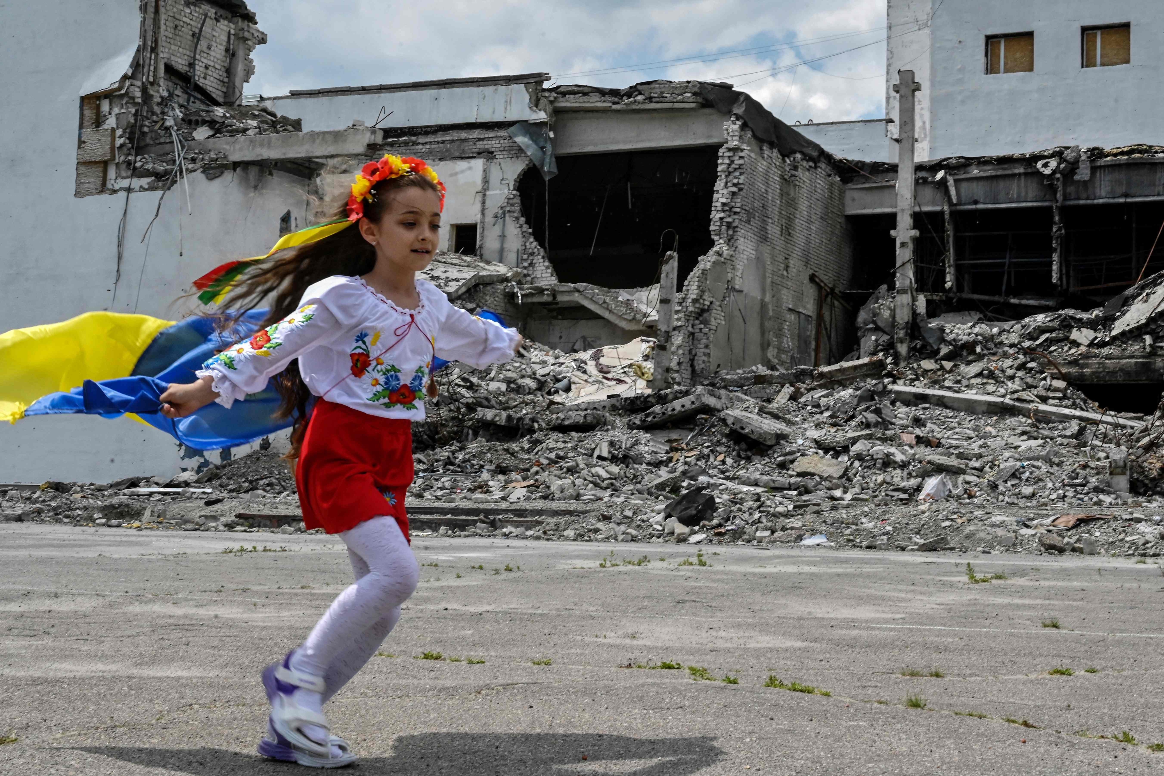 우크라이나 하르키우주 데르하치시의 파괴된 건물 폐허에서 한 소녀가 초등학교 졸업식을 맞아 우크라이나 국기를 어깨에 두른 채 뛰고 있다. 데르하치 AFP 연합뉴스