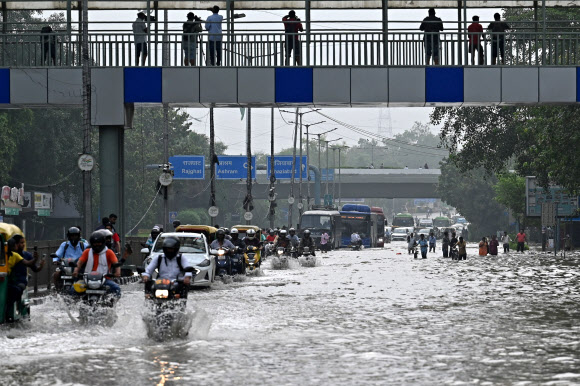 인도 뉴델리 시민들이 14일 몬순 폭우로 인해 야무나 강의 범람으로 물난리가 난 도로를 따라 오토바이 등으로 이동하려 안간힘을 쓰고 있다. 뉴델리 AFP 연합뉴스