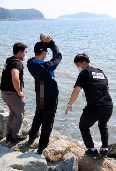 19일 오후 인천시 중구 덕교동 잠진도 제방에서 해경이 바다에 아내를 빠트리고 돌 던져 살해한 혐의를 받는 30대 남편 A씨에 대해 현장 검증에서 A씨가 바다에 빠진 아내에게 돌을 던지는 모습을 재현하고 있다. 2023.7.19 연합뉴스